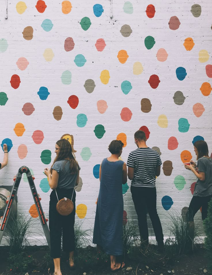 four people are standing in front of a wall with multicolored circles on it