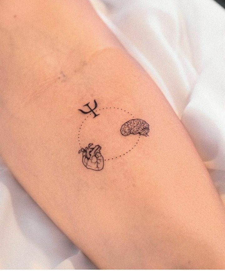 a small heart and brain tattoo on the right side of the left arm, with an arrow pointing to it