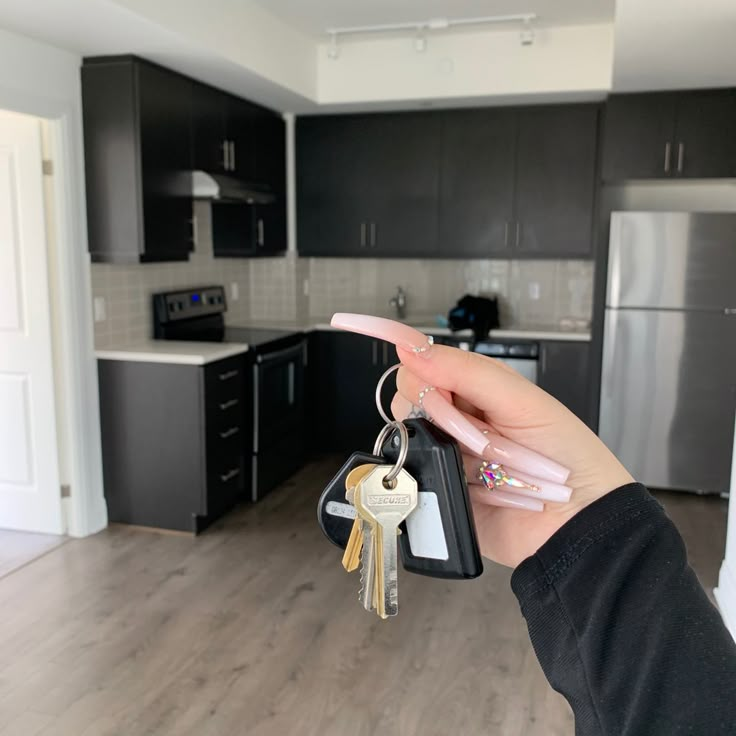 a person holding two keys in front of a kitchen with stainless steel appliances and cabinets