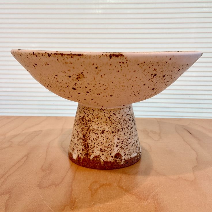 a brown and white bowl sitting on top of a wooden table next to a window