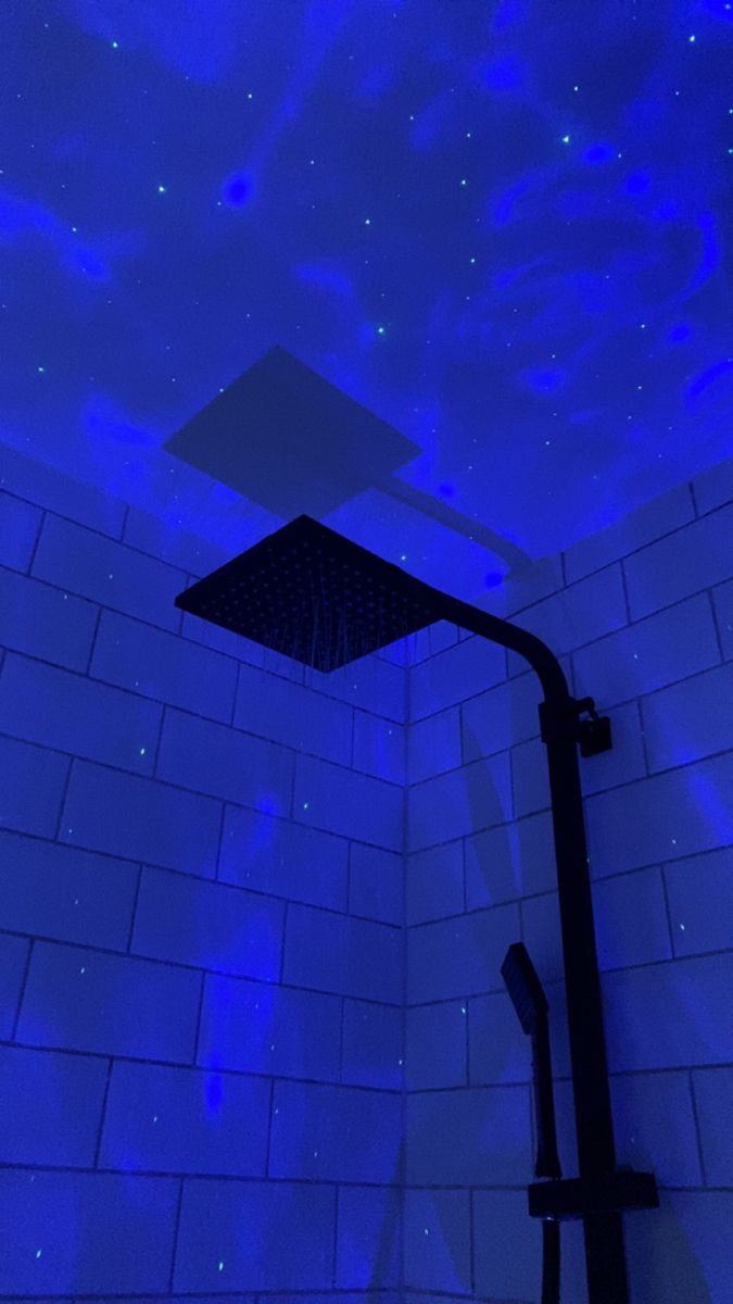 a shower head in the middle of a tiled wall with blue lights shining on it