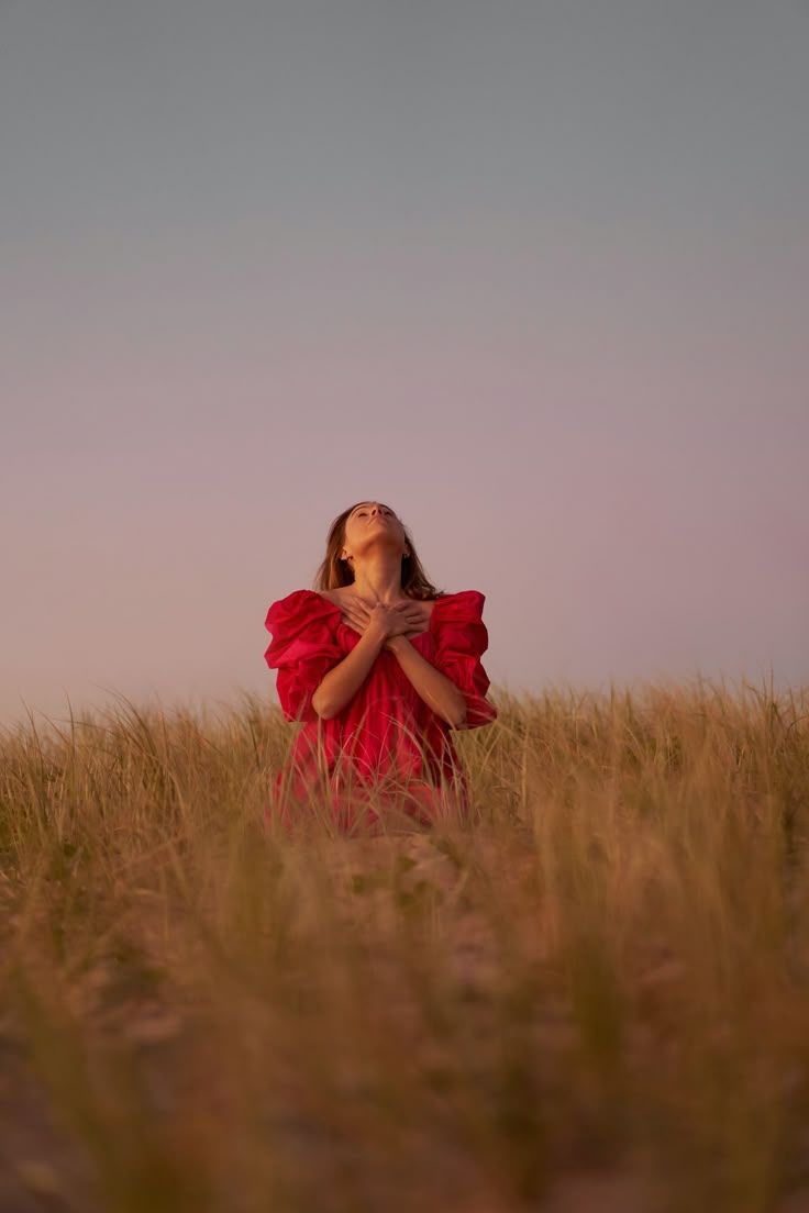 a woman in a red dress is standing in the middle of a field with her eyes closed