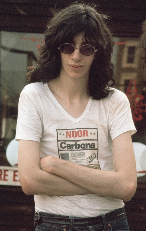 a woman with her arms crossed standing in front of a car and another person wearing sunglasses