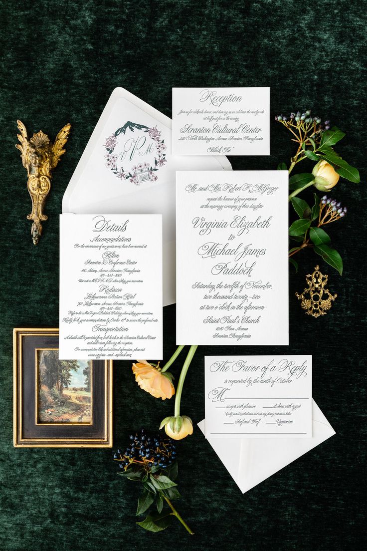 the wedding stationery is laid out on a green velvet surface with flowers and greenery