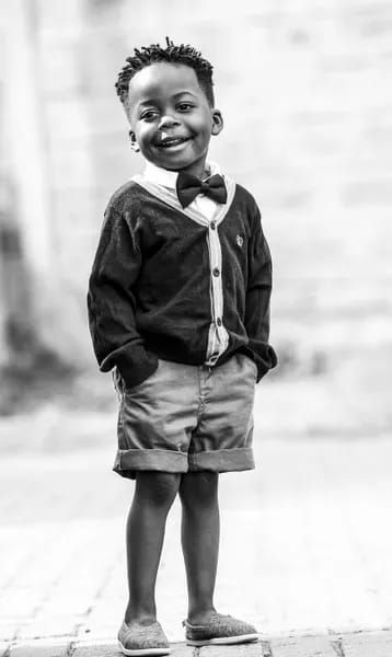 a little boy that is standing up with a bow tie in his hand and smiling