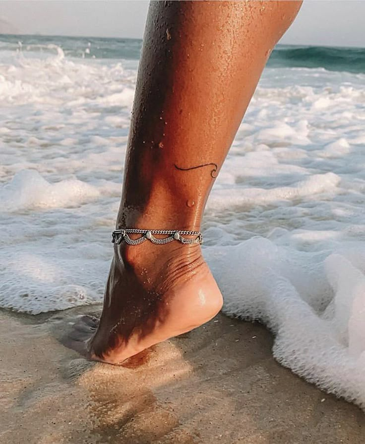 a woman's foot with a tattoo on it walking in the sand at the beach