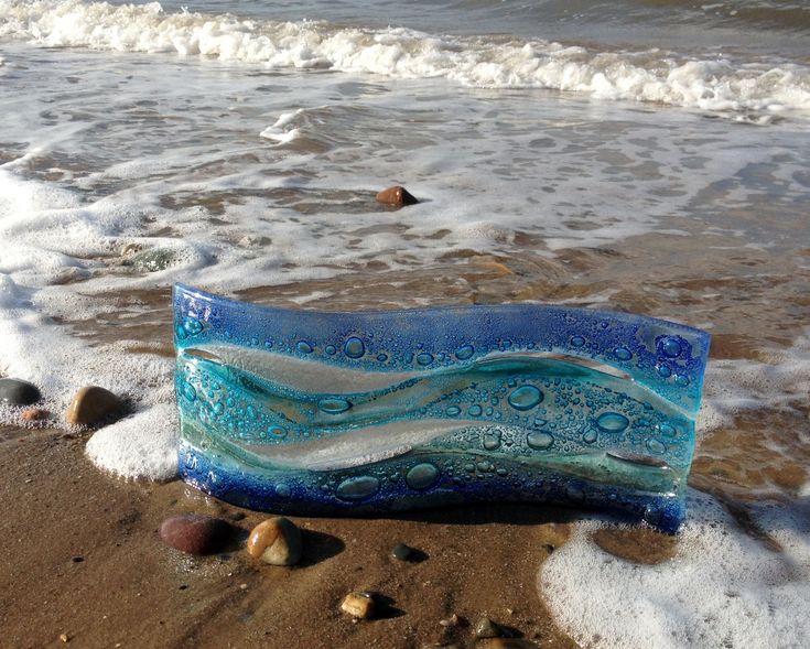 a blue glass object sitting on top of a sandy beach next to the ocean with waves coming in