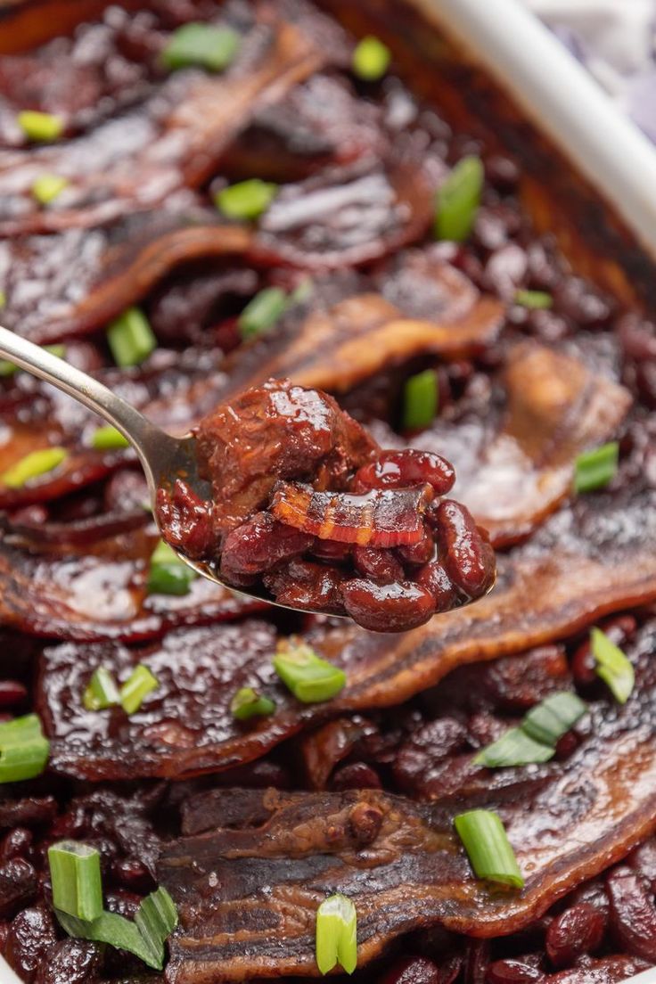 a spoon with food on it is being held by someone's hand over a casserole dish