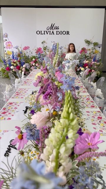 a long table with flowers on it and a woman in the background