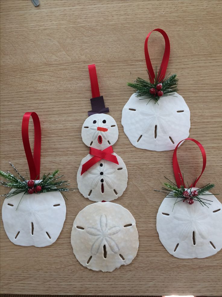 four snowmen made out of sand sitting on top of a wooden table next to red ribbon