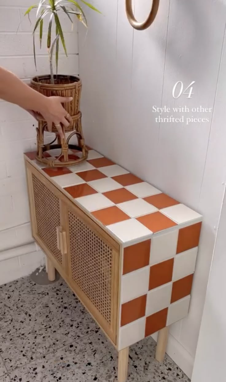 a person reaching for a potted plant on top of a wooden cabinet with an orange and white checkerboard design