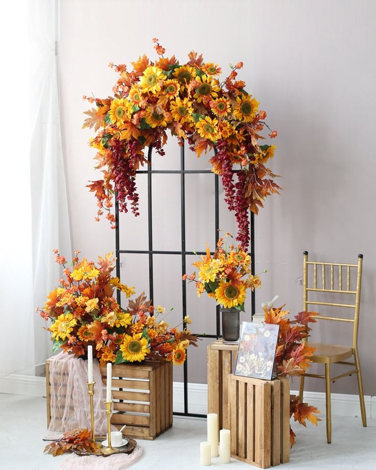 an arrangement of flowers and candles on display in front of a window with fall foliage