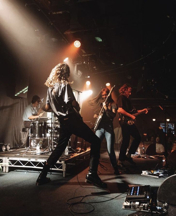 a group of people that are on stage with some lights in the background and one person playing guitar