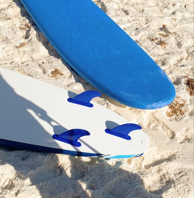 two blue and white surfboards laying in the sand