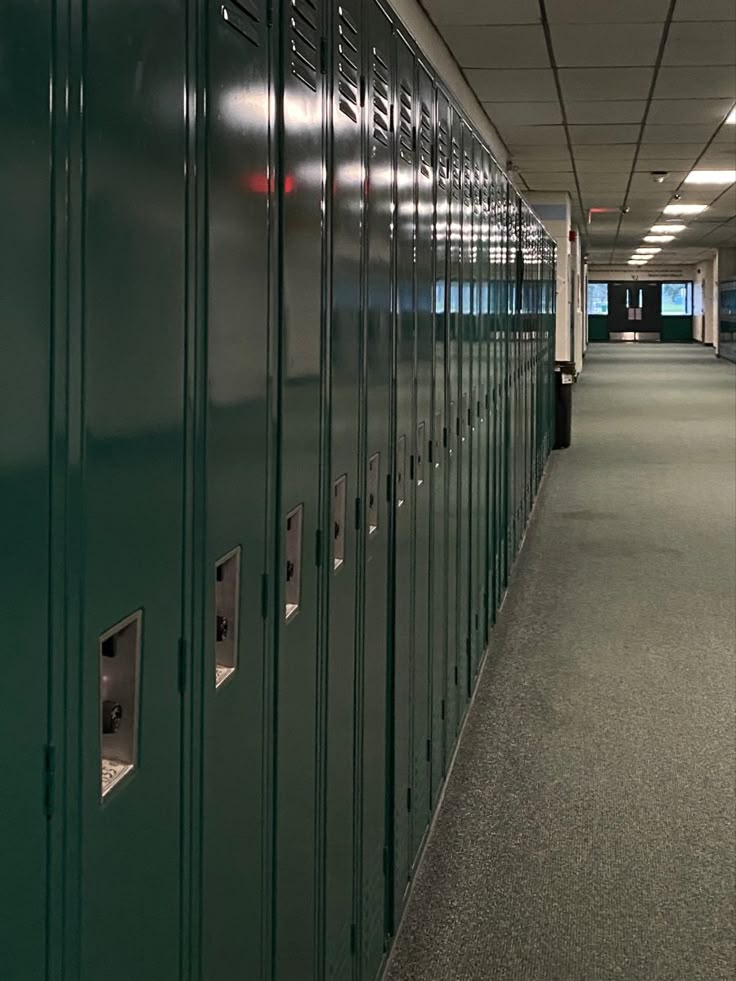 a long row of green lockers in an empty hallway with lights on the ceiling