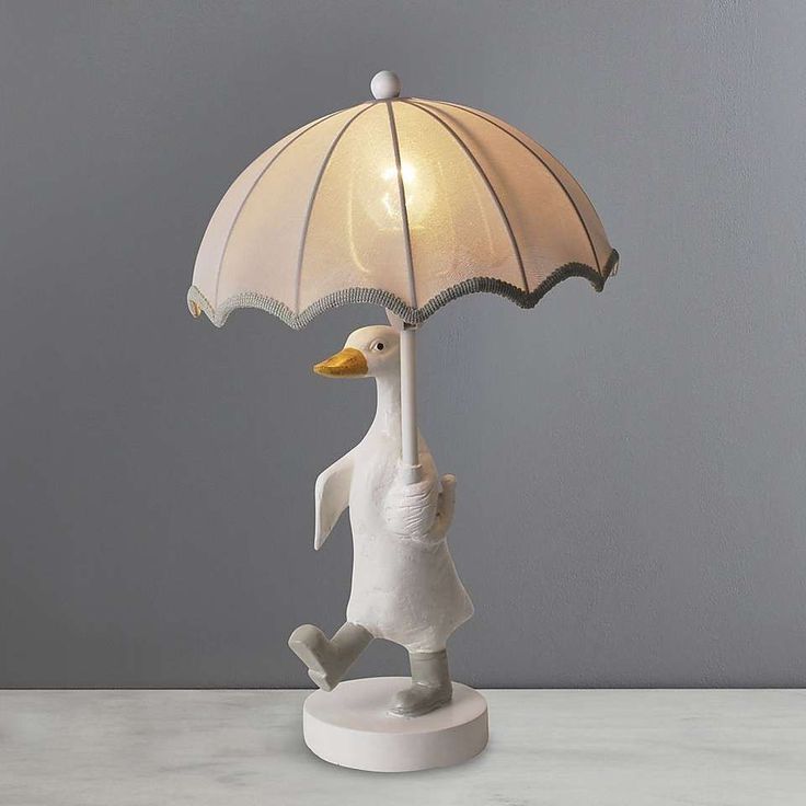 a lamp with a duck holding an umbrella on it's head, sitting on a table