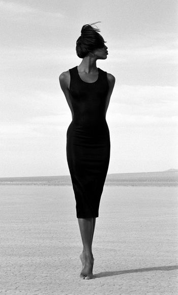 a woman in a black dress walking on the beach