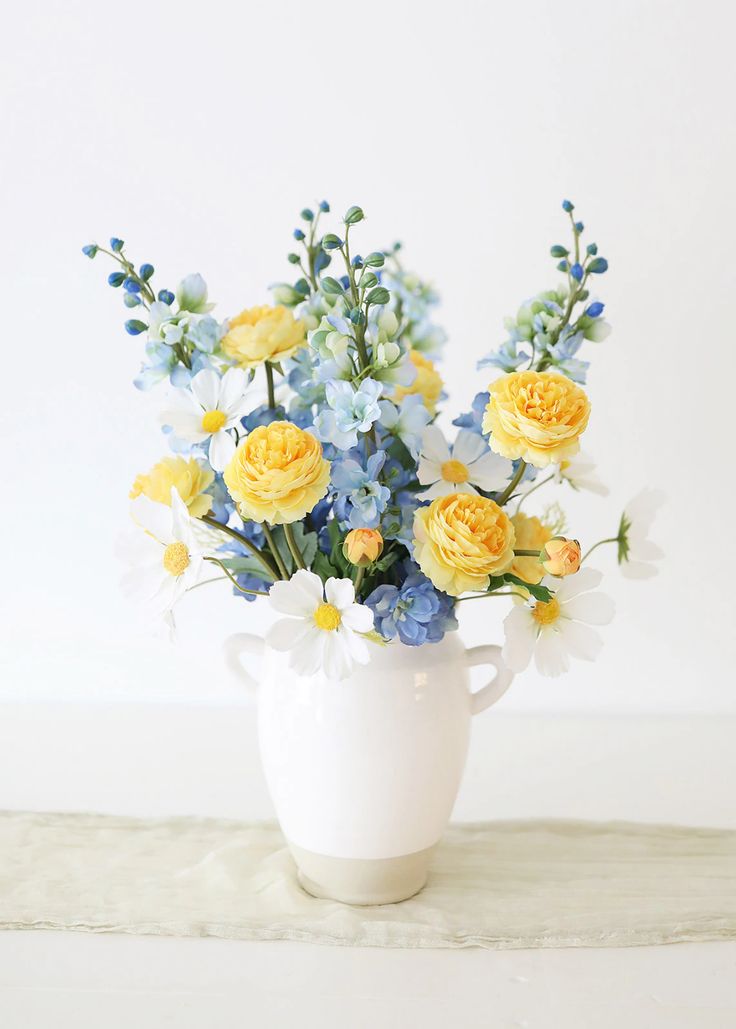 a white vase filled with yellow and blue flowers