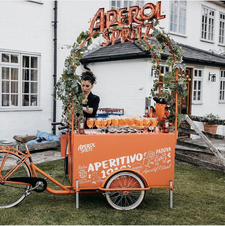 an orange cart selling drinks in front of a white building with the word apricot written on it