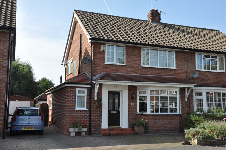 a car is parked in front of a brick house with white windows and two chimneys