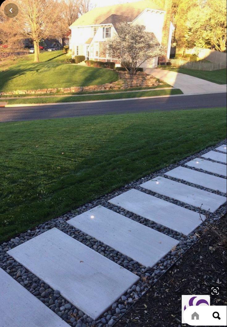 a stone walkway in front of a house on the side of a road with grass