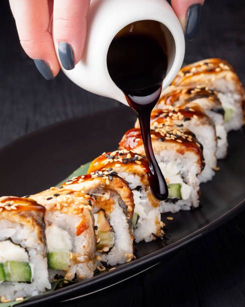 someone is pouring sauce on some sushi