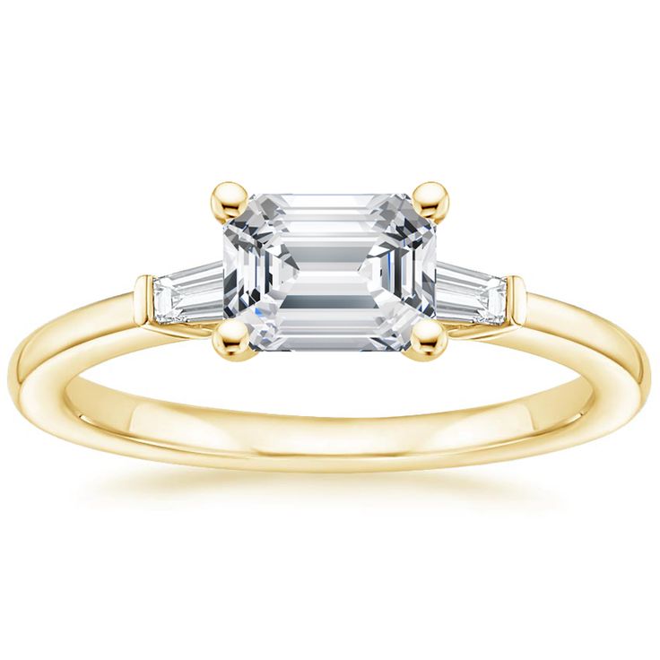 a yellow gold engagement ring set with an emerald and baguette cut diamond in the center