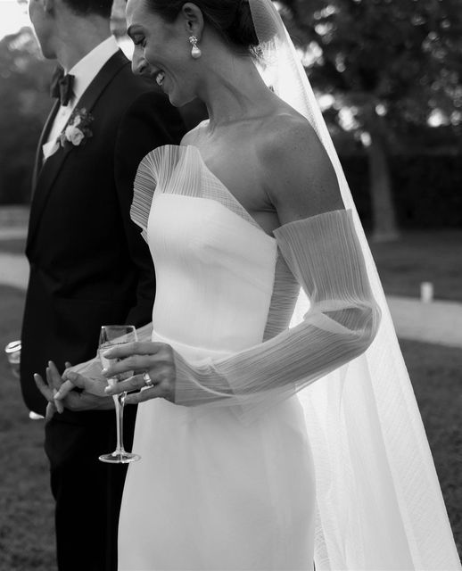 a bride and groom standing next to each other holding wine glasses in front of them