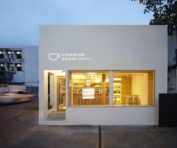 a small white building with windows and lights on the outside, next to a parking lot