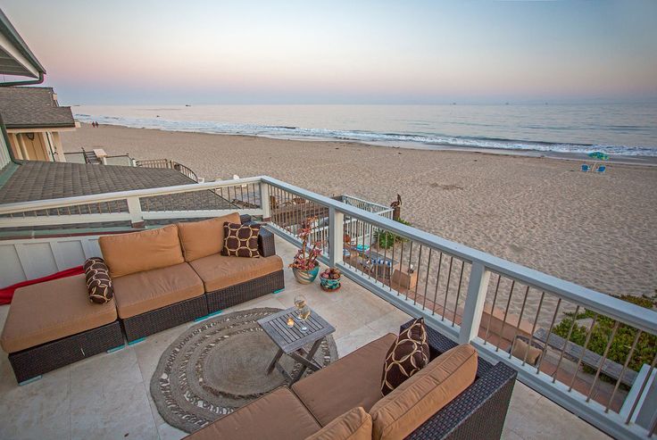 a balcony with couches and tables on the side of it next to the beach