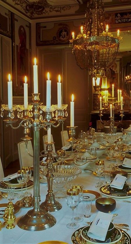 a long table is set with gold plates and silver place settings, candles in the middle