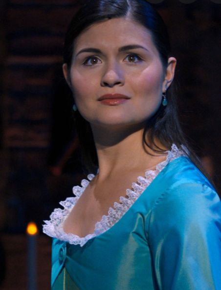 a woman in a blue dress standing next to a candle lit room and looking off into the distance