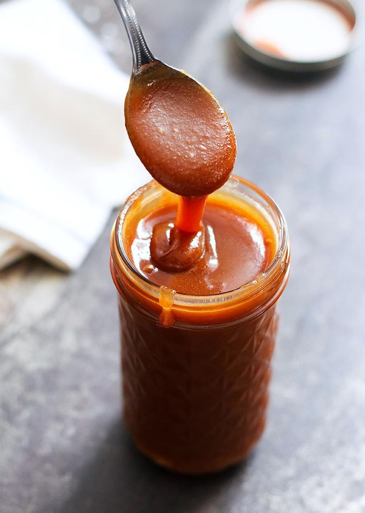 a spoon full of peanut butter on top of a glass jar filled with chocolate sauce