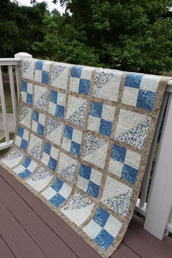 a blue and white quilt hanging on the side of a wooden deck next to trees