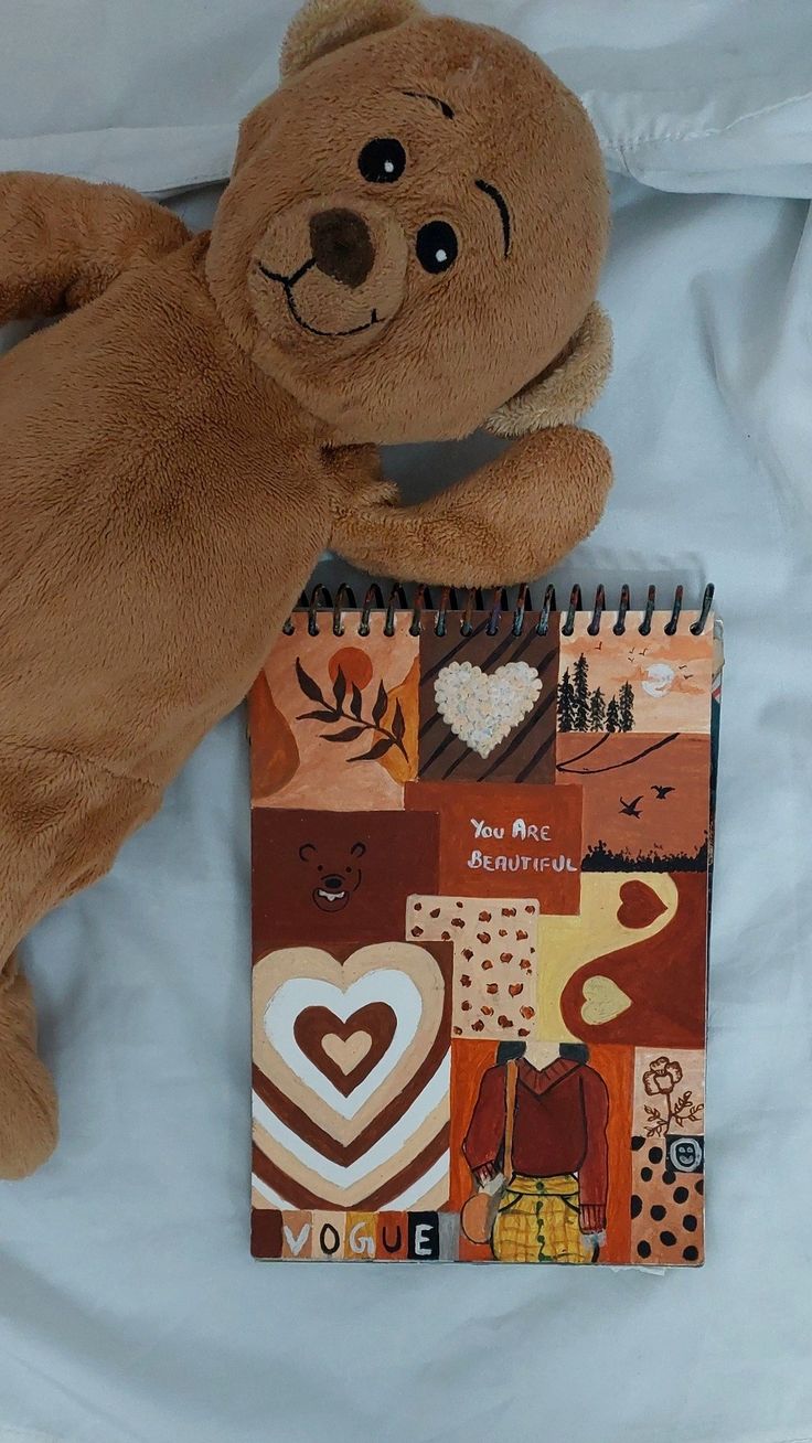 a brown teddy bear laying on top of a bed next to a notebook