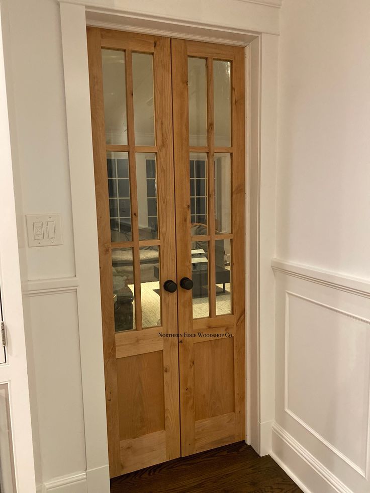 an empty room with two wooden doors and hard wood flooring on the side walk