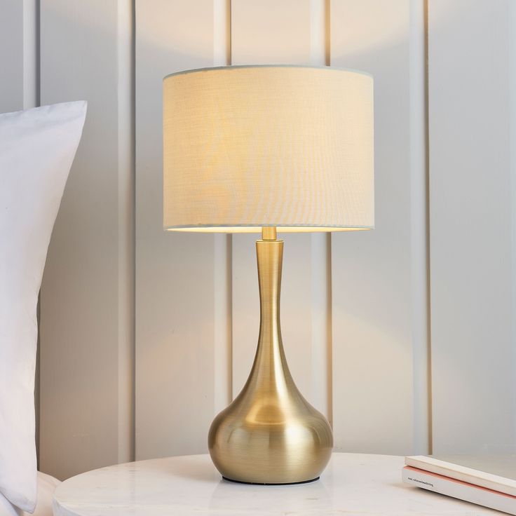 a gold lamp sitting on top of a white table next to a book and pillow