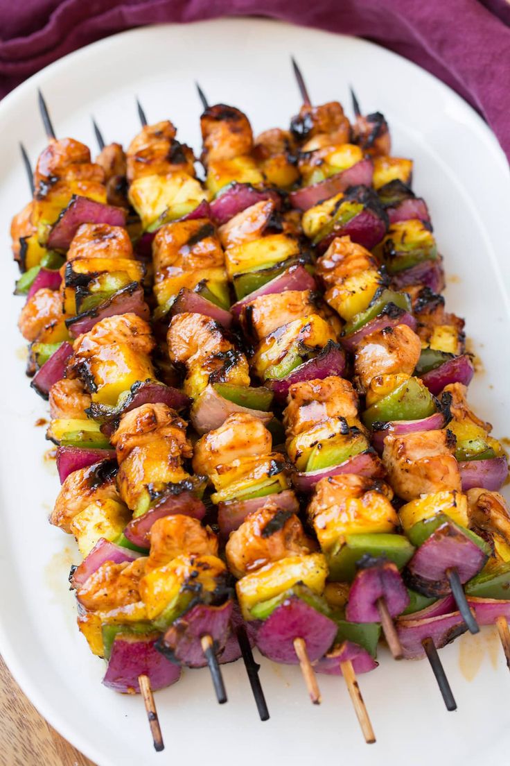 skewered vegetables and meat on a white plate with purple cloth next to it