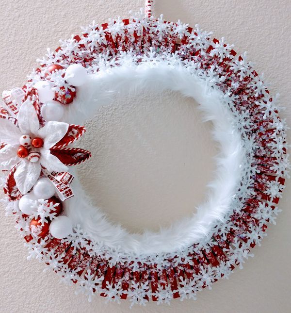 a white wreath with red and white decorations hanging on a wall next to a candle