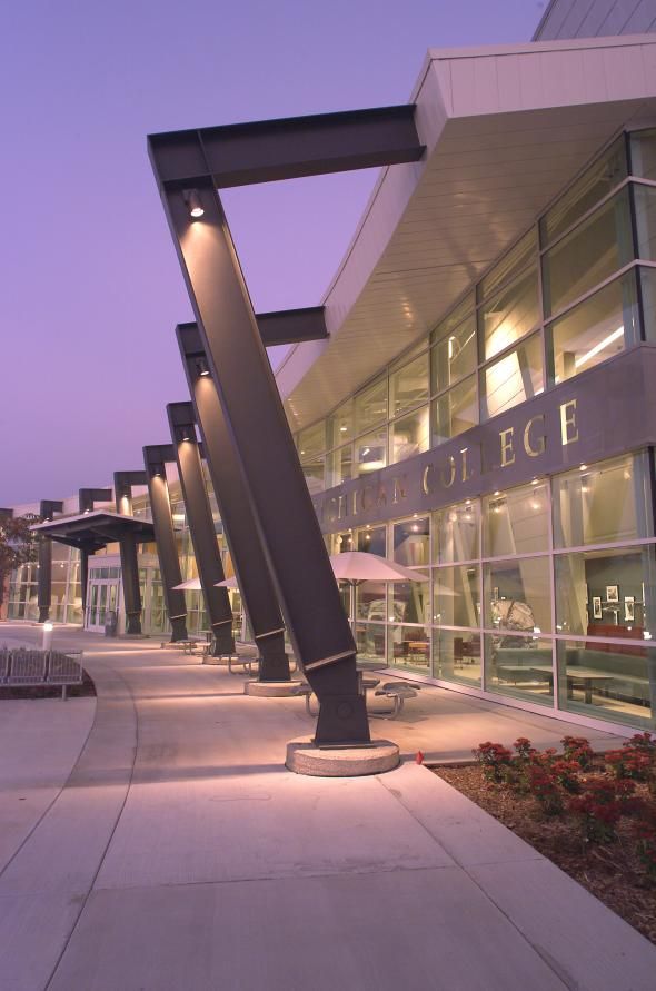 an empty sidewalk in front of a large building with many windows and lights on it