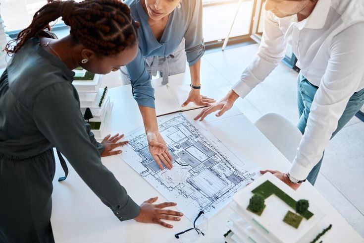 three people looking at a blueprint on top of a white table in an office