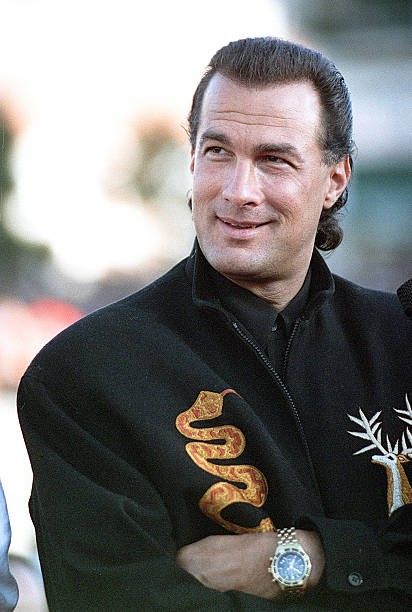 a man with his arms crossed wearing a black jacket and gold embroidered snake on it