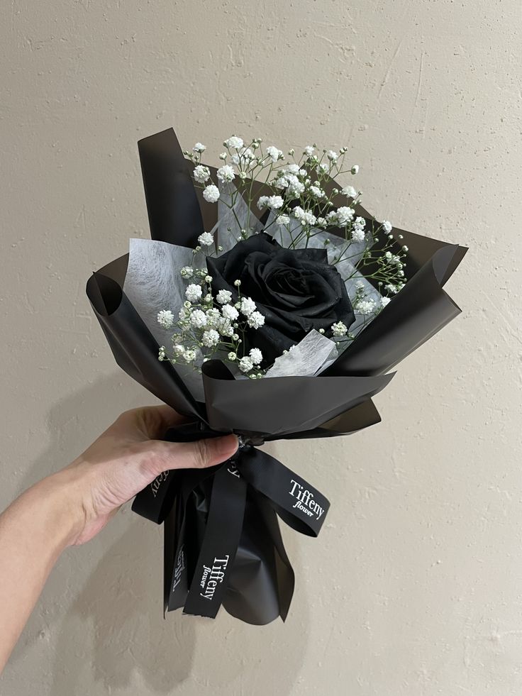 a hand holding a bouquet of flowers with black ribbon and white baby's breath