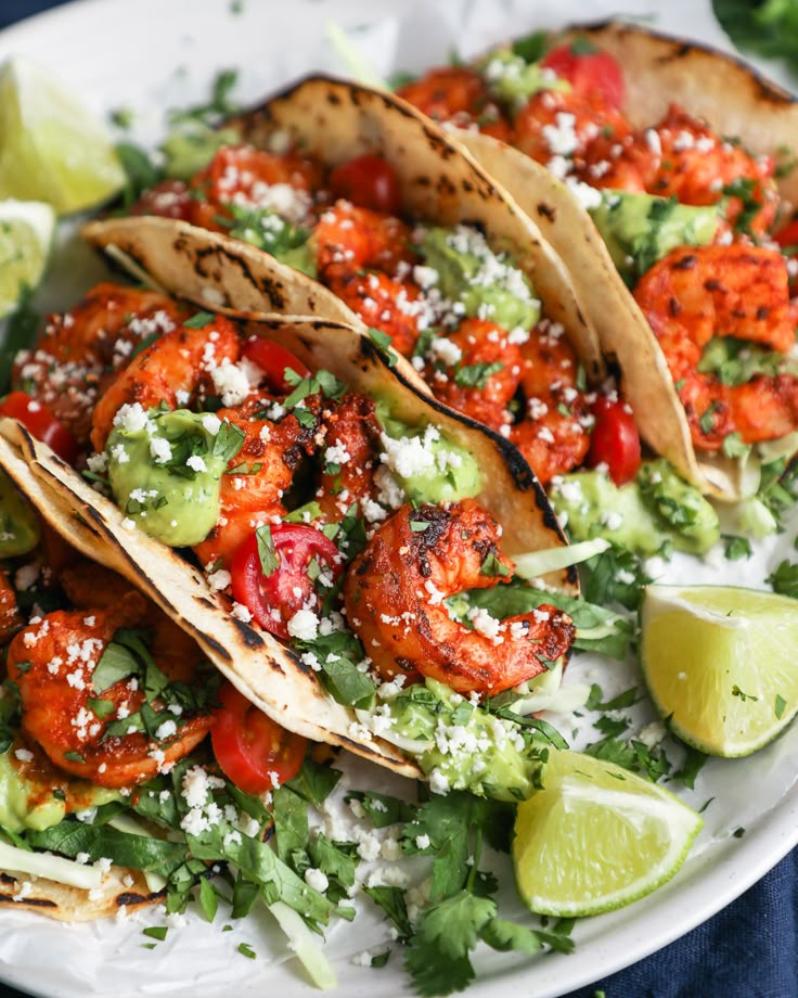 three tacos on a white plate with limes and cilantro wedges