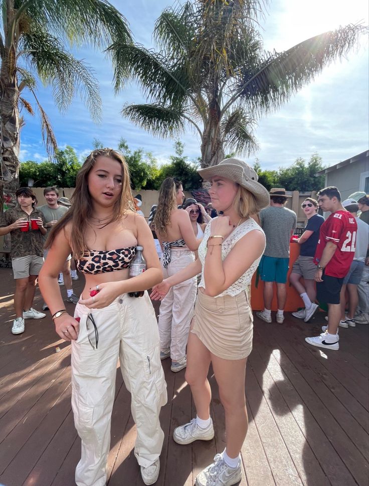 two young women standing next to each other on a wooden deck with palm trees in the background