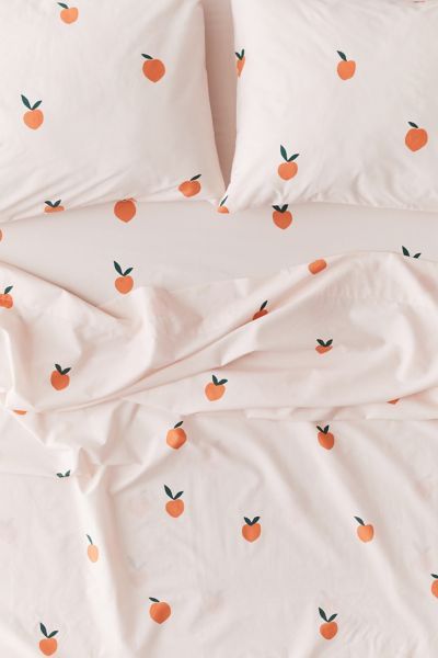 an unmade bed with white sheets and oranges printed on the pillowcase, along with two pillows