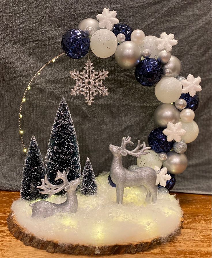 a christmas wreath with silver and white ornaments on top of snow covered ground next to trees