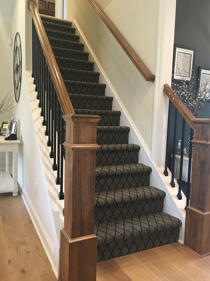 a stair case with black and white carpet on the bottom, and wooden handrails