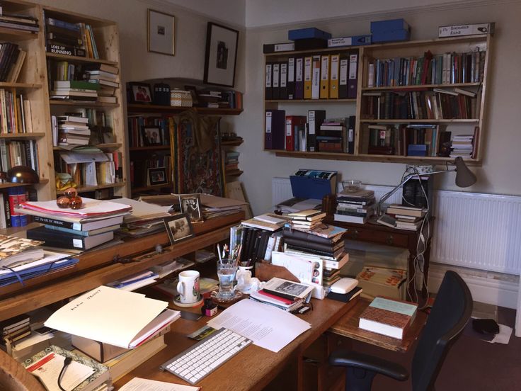 a desk with many books and papers on top of it in front of a bookcase