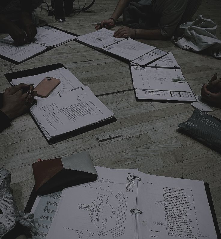 several people sitting on the floor with papers and pens in front of them, while one person is writing